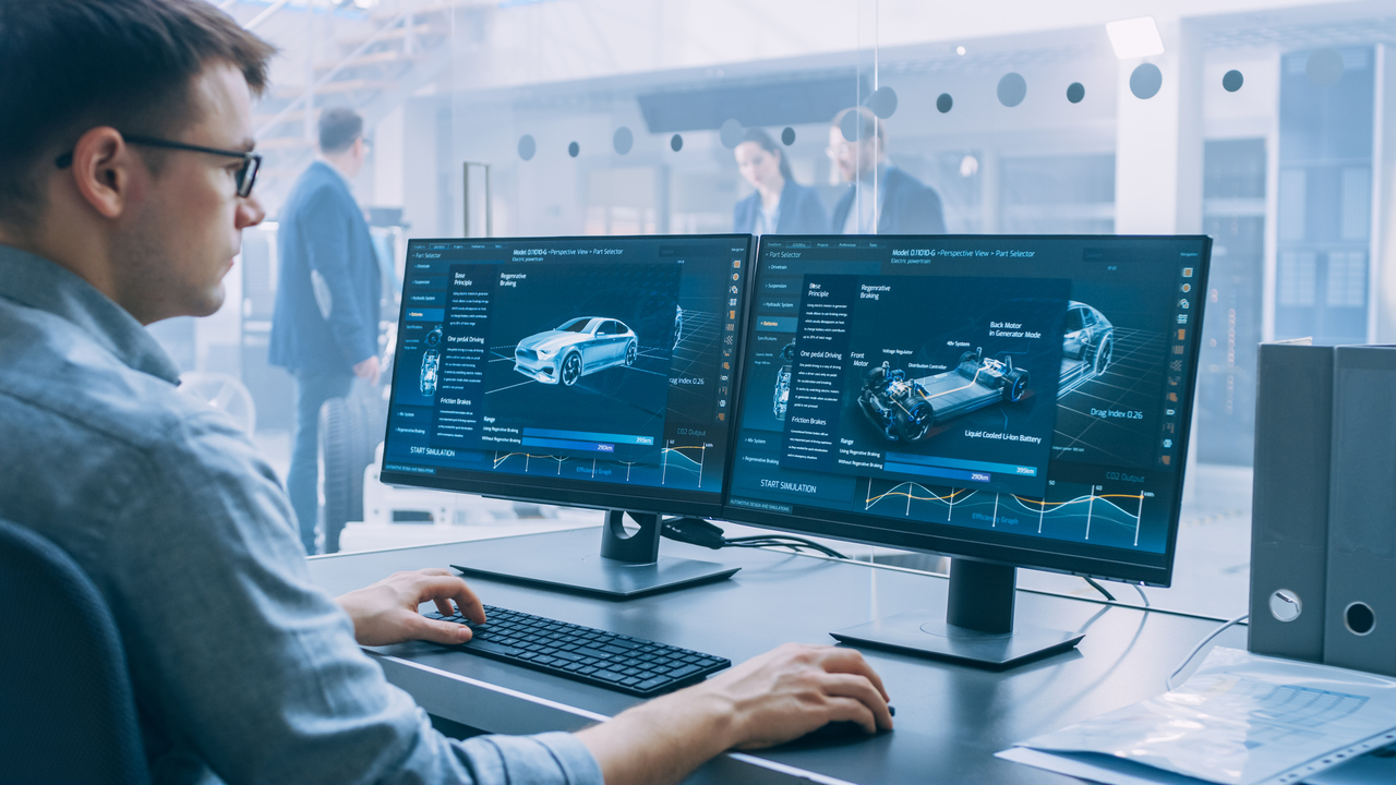 Mitarbeiter arbeitet an zwei Monitoren mit digitaler Fahrzeugsimulation und Analyse-Dashboard