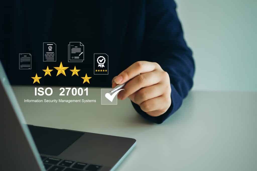 Person setzt ein Häkchen bei ISO 27001, umgeben von Symbolen für Informationssicherheitsmanagement, Audit und Zertifizierung.